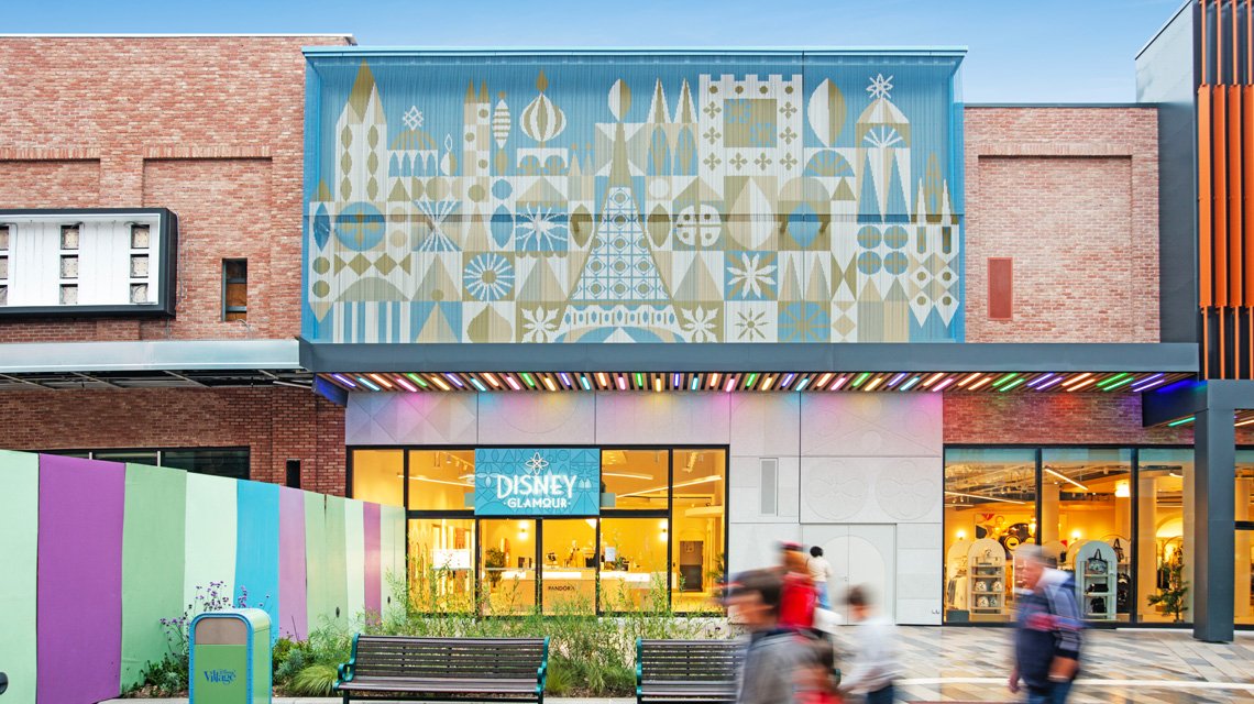 Façade Kriskadecor Disney Village – Vue large intégrée au commerce - <p>Vue large de la façade Kriskadecor couvrant l’entrée d’un commerce du Disney Village. L’image montre l’intégration du panneau en chaînes aluminium dans l’environnement piéton, soulignant son rôle de signalétique architecturale et d’habillage décoratif extérieur.</p>