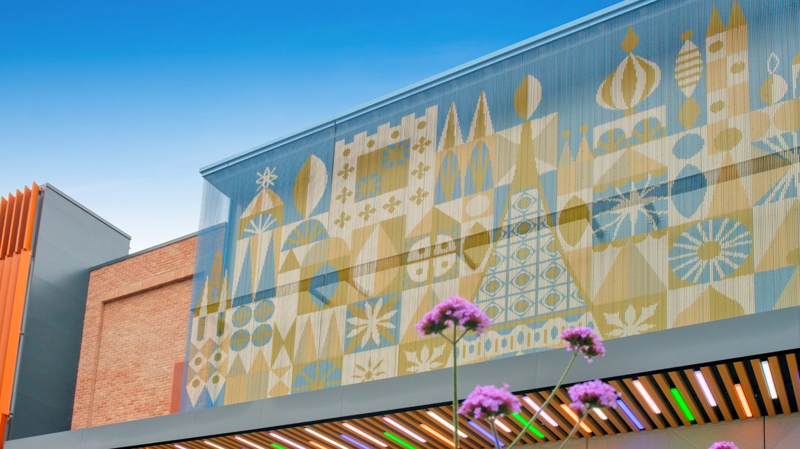 Façade métallique Kriskadecor Disney Village – Vue diagonale complète - <p>Vue diagonale de l’habillage de façade en chaînes aluminium Kriskadecor au Disney Village (Disneyland Paris). La perspective met en valeur le rendu tridimensionnel du rideau de maillons anodisés et l’intégration du décor graphique dans l’architecture retail.</p>