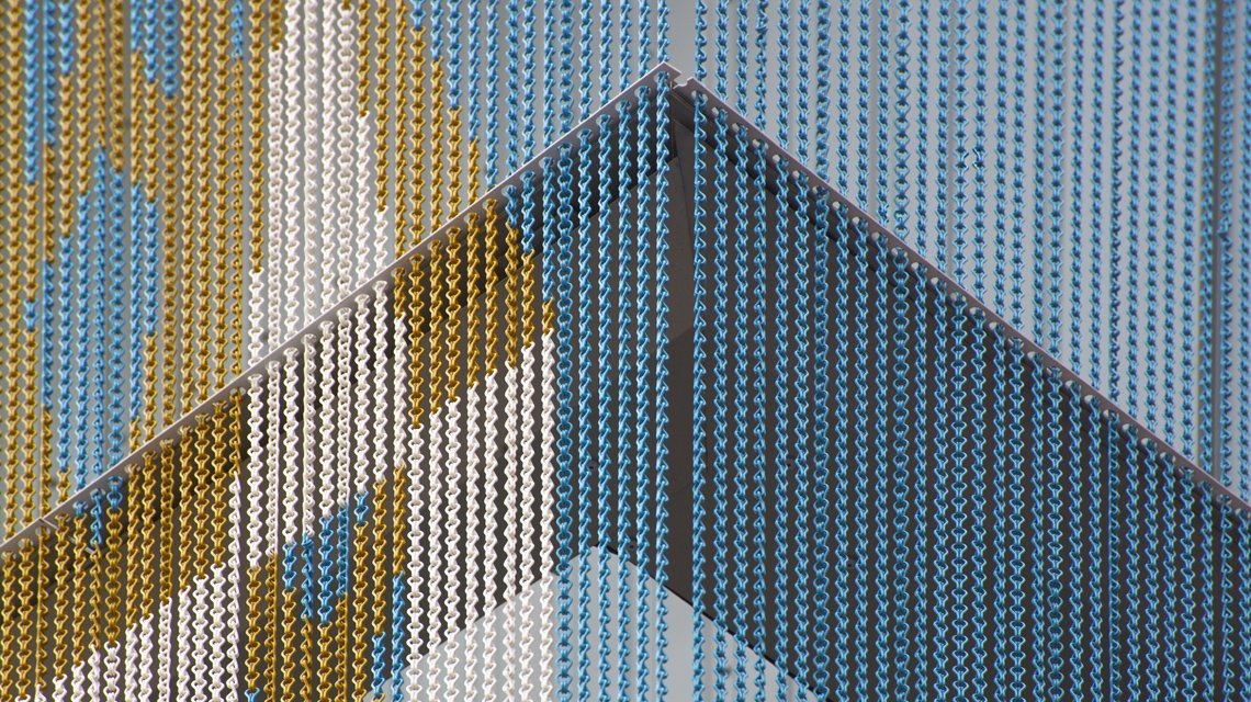 Transition graphique sur chaînes aluminium – Détail Kriskadecor - <p>Zoom diagonal montrant la transition des formes et des couleurs sur les maillons Kriskadecor. Ce type de détail illustre la capacité du matériau à reproduire des motifs complexes pour les projets architecturaux.</p>