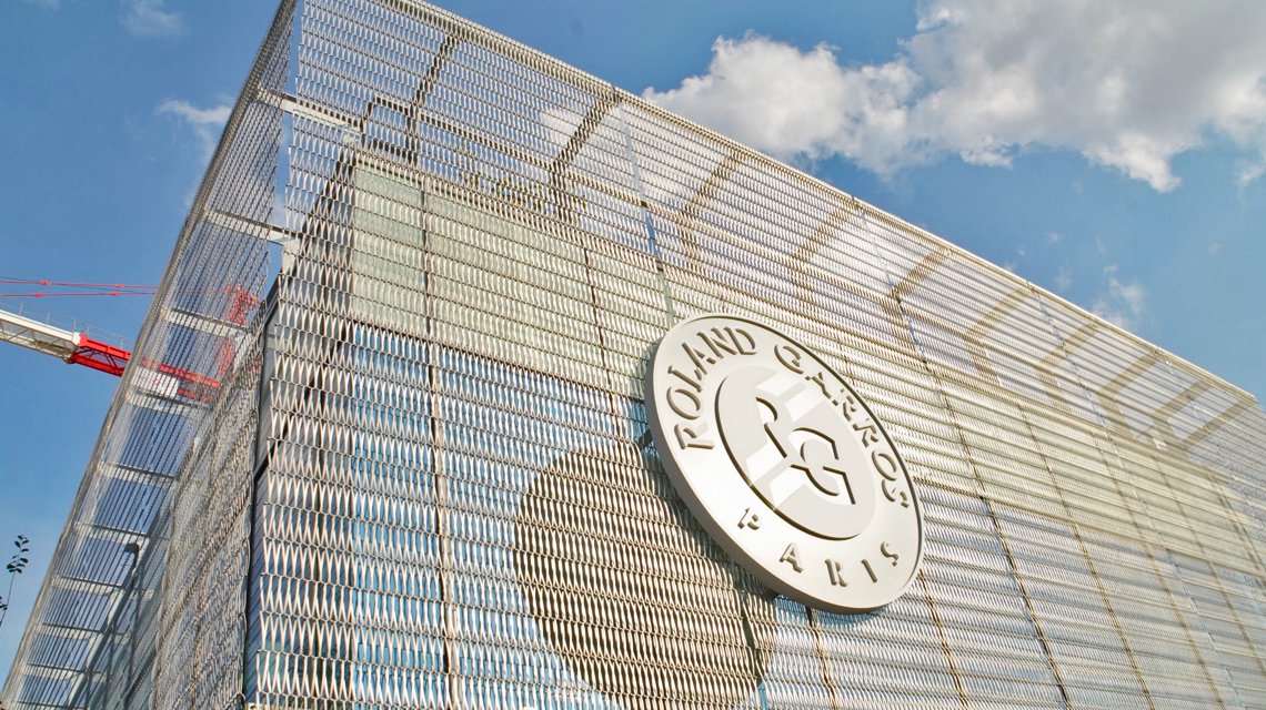 Façade en maille métallique – Logo Roland Garros - <p>Façade architecturale du site Roland Garros habillée en maille métallique spiralée, avec le logo emblématique du tournoi intégré sur la double-peau en inox EIFFEL30150, fabriquée par Codina Architectural.</p>