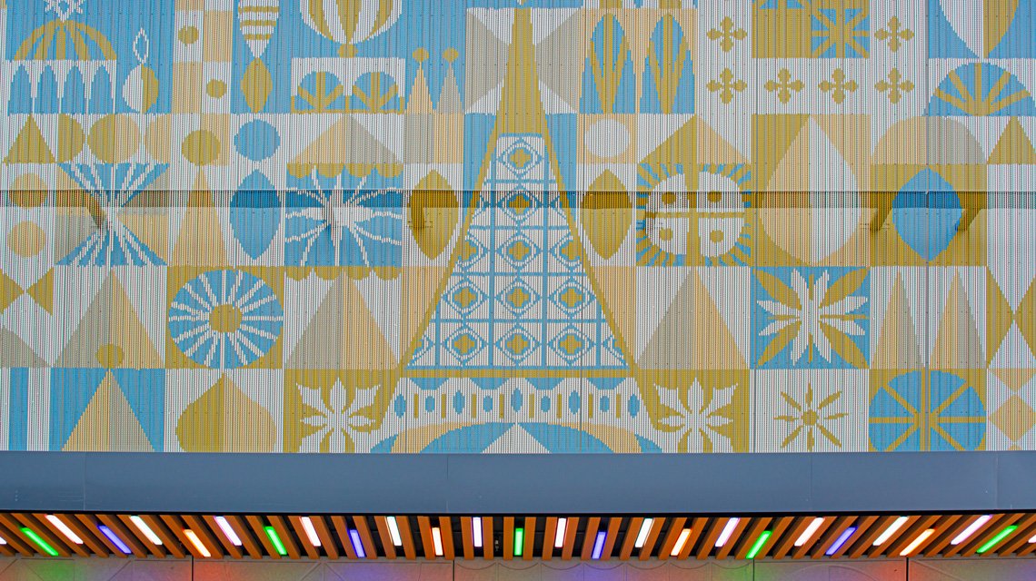 Façade Kriskadecor Disney Village – Détail bandeau central - <p>Vue rapprochée du bandeau central de la façade en chaînes aluminium Kriskadecor installée au Disney Village. L’image révèle la précision du motif géométrique reproduit sur maillons anodisés bleu et or, démontrant les capacités du système pour les façades décoratives de grande échelle dans les environnements commerciaux.</p>