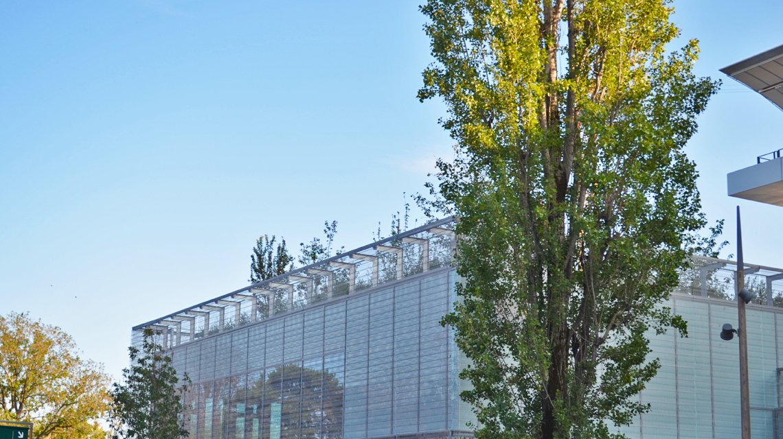 Façade métallique EIFFEL30150 – Jeux d'ombres naturelles - <p>Large façade en maille métallique spiralée EIFFEL30150 qui filtre la lumière et laisse apparaître les ombres des arbres, jouant un rôle de double-peau architecturale pour les bâtiments du Village Roland Garros.</p>